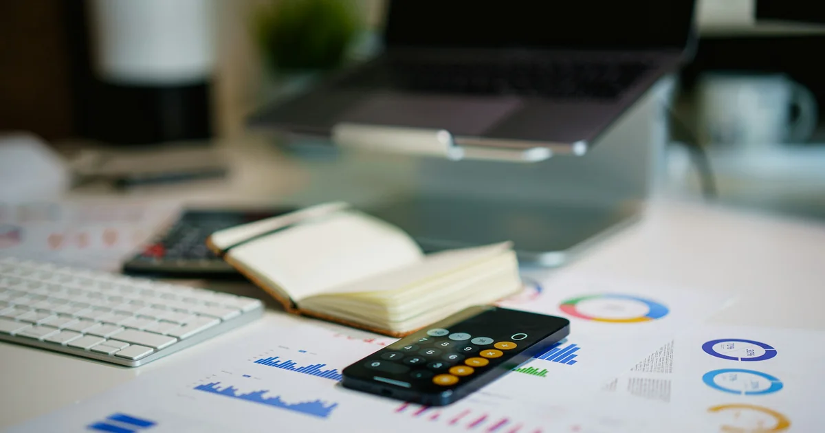 Office desk with a notebook, a smartphone calculator and financial charts